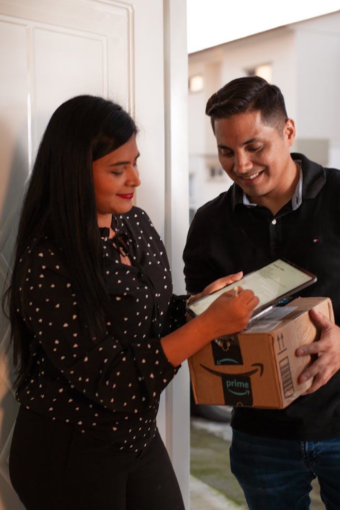 A man receives a package from a delivery person who is assisting with a digital signature.