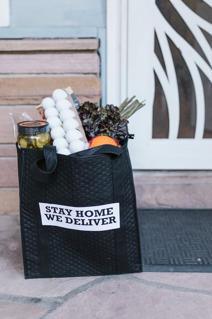 Reusable grocery bag with fresh produce and eggs on doorstep during stay-at-home delivery.